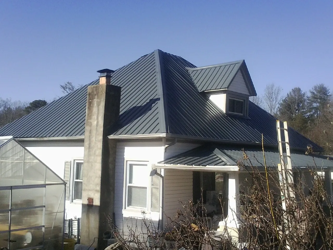 Dark blue standing seam metal roof on a white farmhouse with dormer — Slate & Tile Roof Repair by Roofing Brothers in Kennard