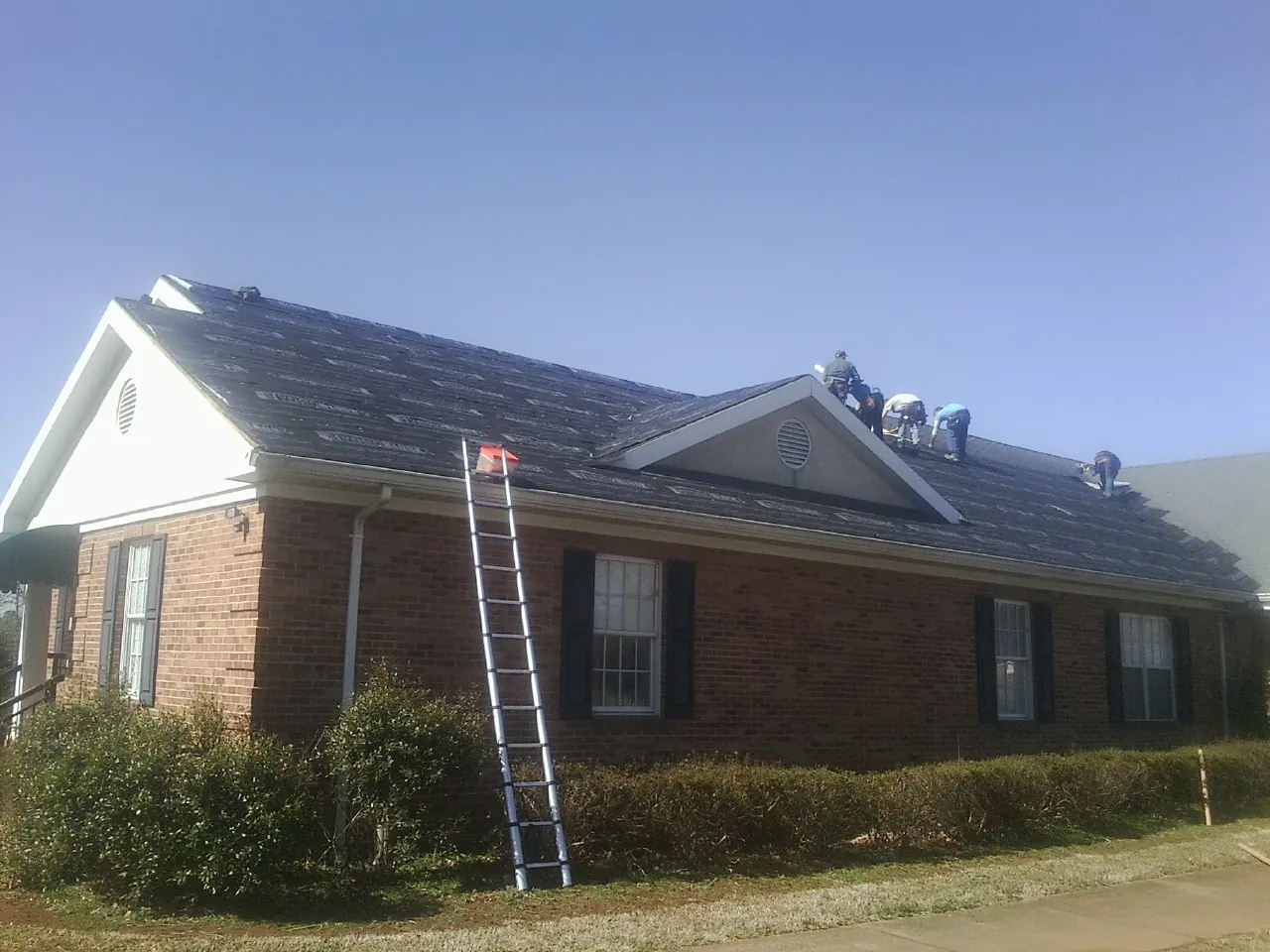 Crew tearing shingles off a brick ranch roof with a ladder set — Emergency Roof Repair work by our crew in Kennard