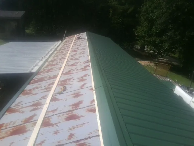 Old rusted panels beside newly installed green metal roofing — Wind Damage Roof Repair by Roofing Brothers in Kennard