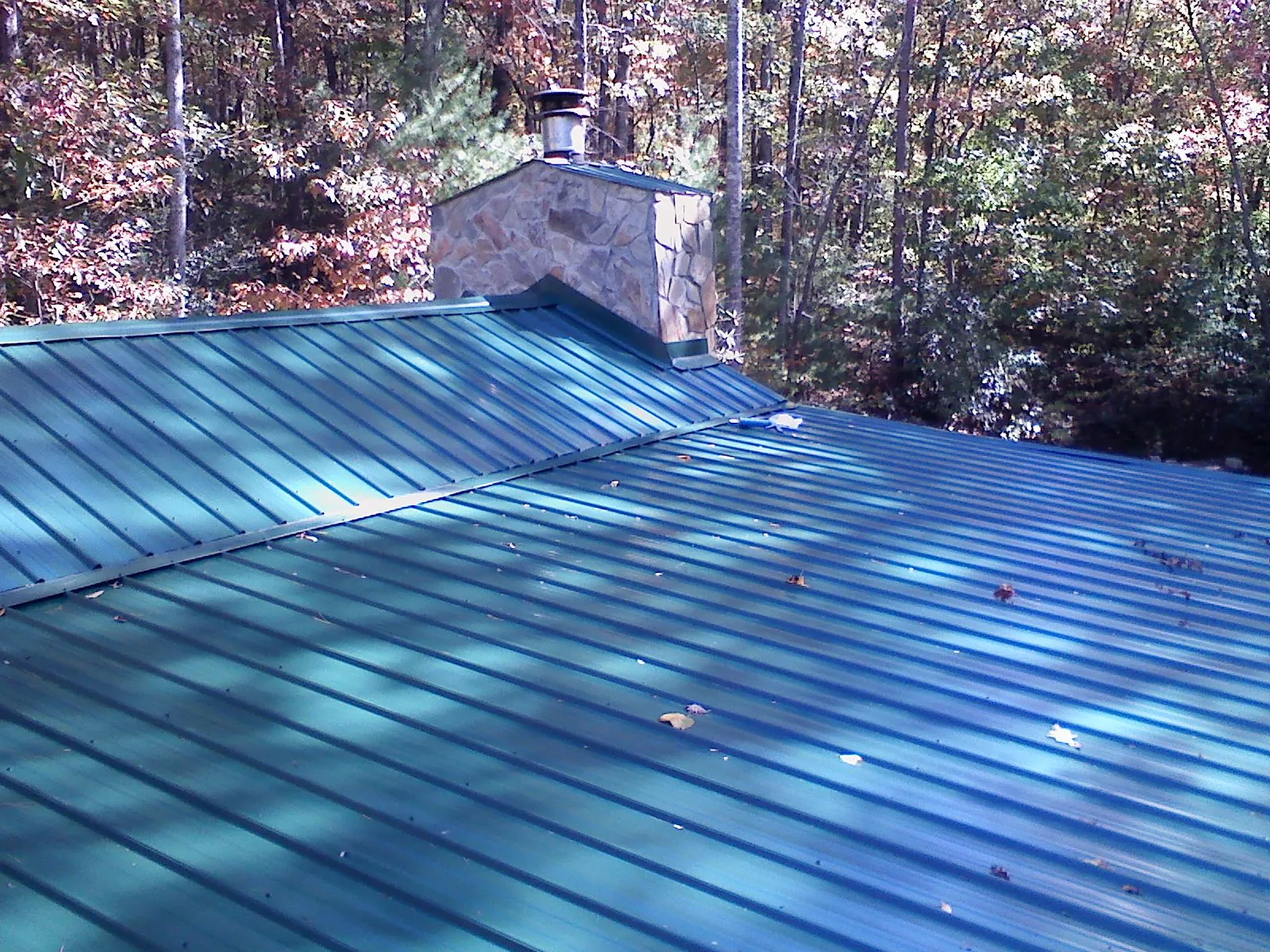 New green metal roof and stone chimney surrounded by autumn woods in Kennard